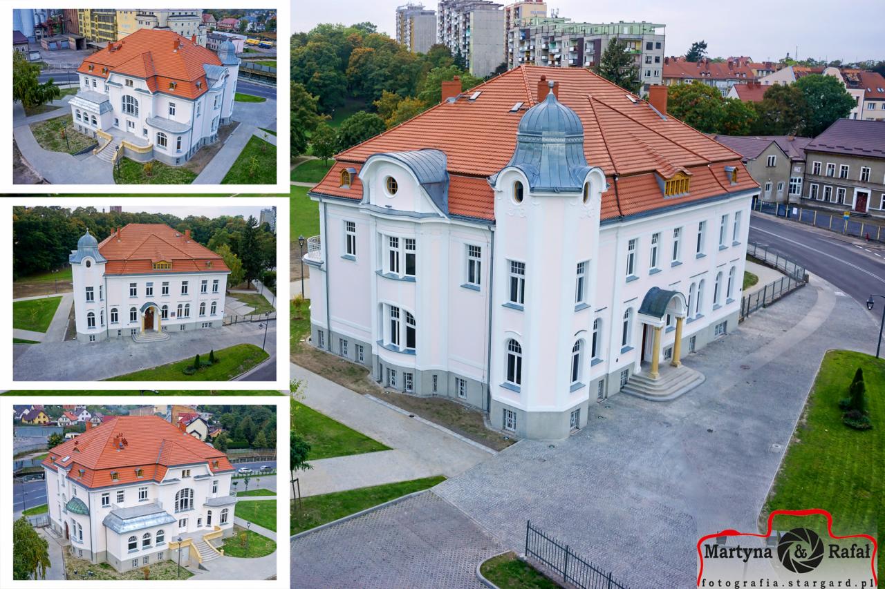 Zdjęcie lotnicze odnowionego, dwupiętrowego budynku z pomarańczową dachówką i jasną elewacją, otoczonego zielenią i chodnikami z kostki brukowej.