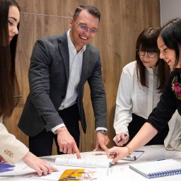 Centrum Ubezpieczeń PARTNER - Cztery osoby analizują dokumenty na stole w biurze, mężczyzna w szarej marynarce uśmiecha się, wskazując na otwartą broszurę.