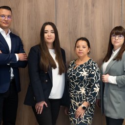 Centrum Ubezpieczeń PARTNER - Czteroosobowy zespół w formalnym stroju pozuje na tle drewnianej ściany, prezentując profesjonalizm i zaufanie.