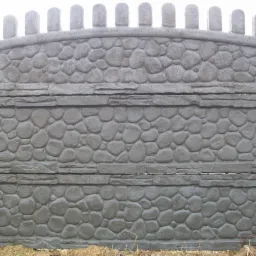 Szary panel ogrodzeniowy z betonową fakturą imitującą kamień, zwieńczony dekoracyjnymi elementami w kształcie baszty, widok frontalny.