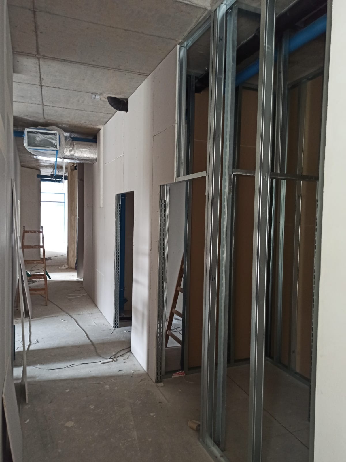 Korytarz w trakcie montażu ścian działowych z płyt gipsowo-kartonowych na metalowym stelażu. Widoczne instalacje i drabina. Surowy betonowy sufit.