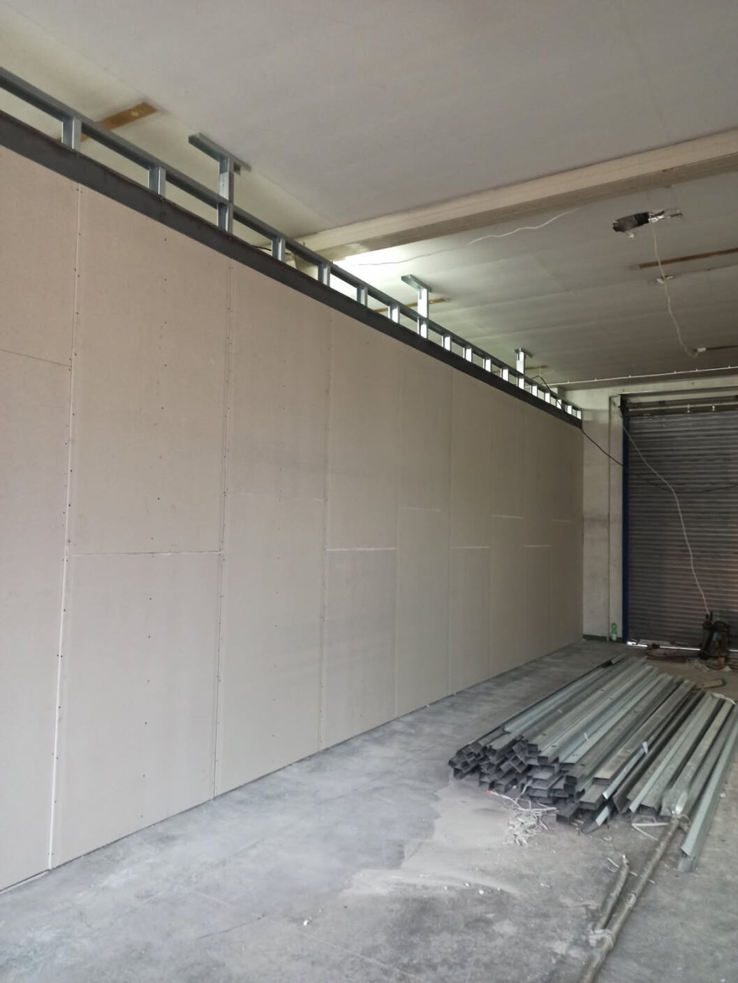 Montaż ścian z płyty karton-gips na metalowym stelażu w surowym wnętrzu. Widoczne profile i płyty przed szpachlowaniem. Surowy beton na podłodze.