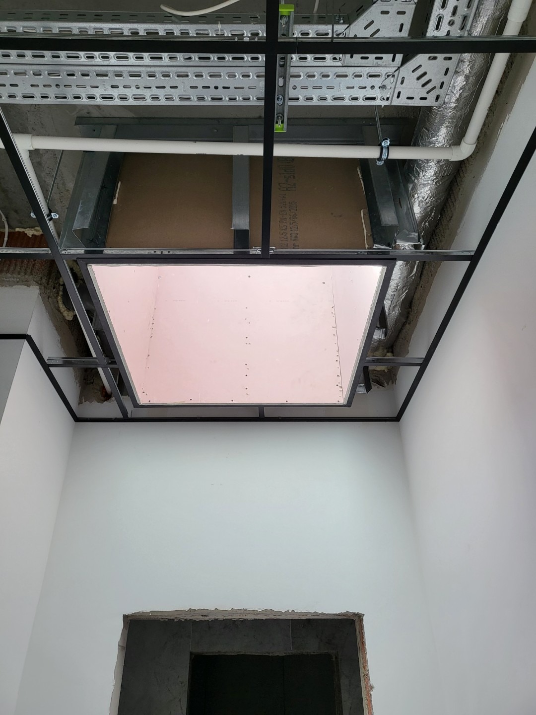 Montaż sufitu podwieszanego z płyty karton gips w biurze, widoczne stalowe profile, instalacje pod sufitem i fragment ściany z otworem drzwiowym.