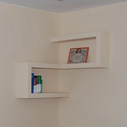 Gama - Białe, narożne półki z płyty karton gips, podświetlane od góry, na ścianie w jasnym odcieniu beżu, na jednej półce książki, na drugiej oprawiony obrazek.