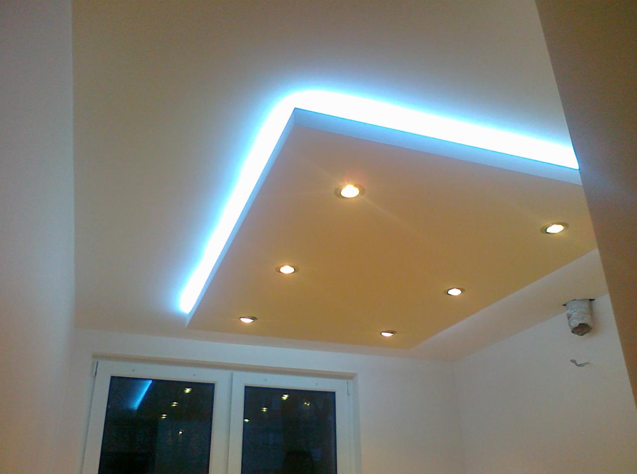 Podwieszany sufit z oświetleniem LED po obwodzie i sześcioma punktowymi lampami w kwadratowej wnęce, widok z dołu na tle okna.