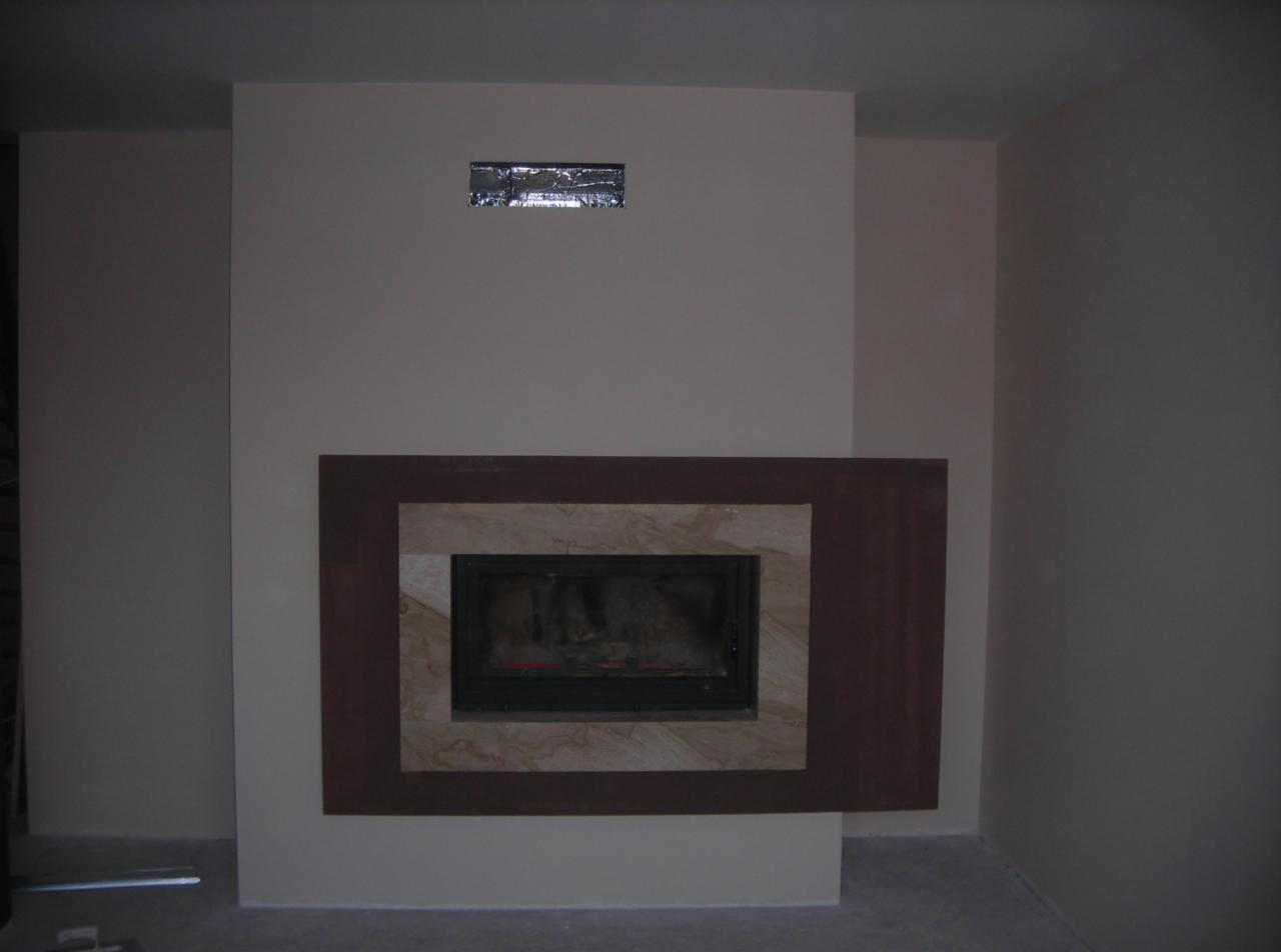 Ściana z wnęką na kominek w trakcie wykończenia, widoczna izolacja nad kominkiem i surowy beton na podłodze.