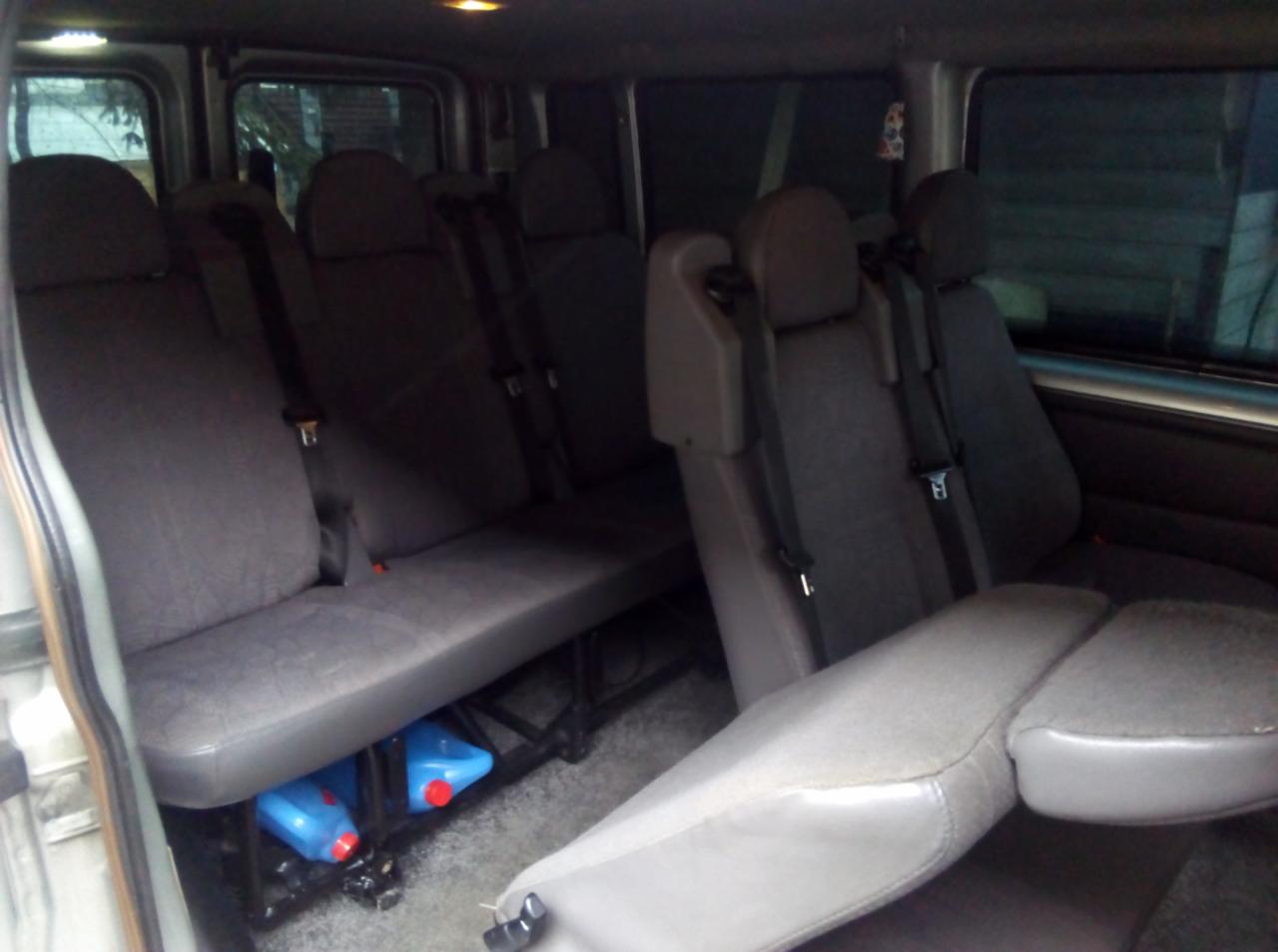 Wnętrze mikrobusu z trzema rzędami siedzeń, pod jednym z nich widoczne pojemniki z płynem do spryskiwaczy.