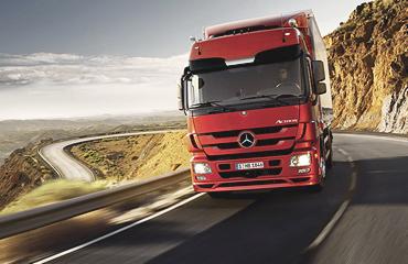 Czerwona ciężarówka Mercedes-Benz Actros na krętej górskiej drodze, widok z niskiej perspektywy podkreślający dynamikę pojazdu.