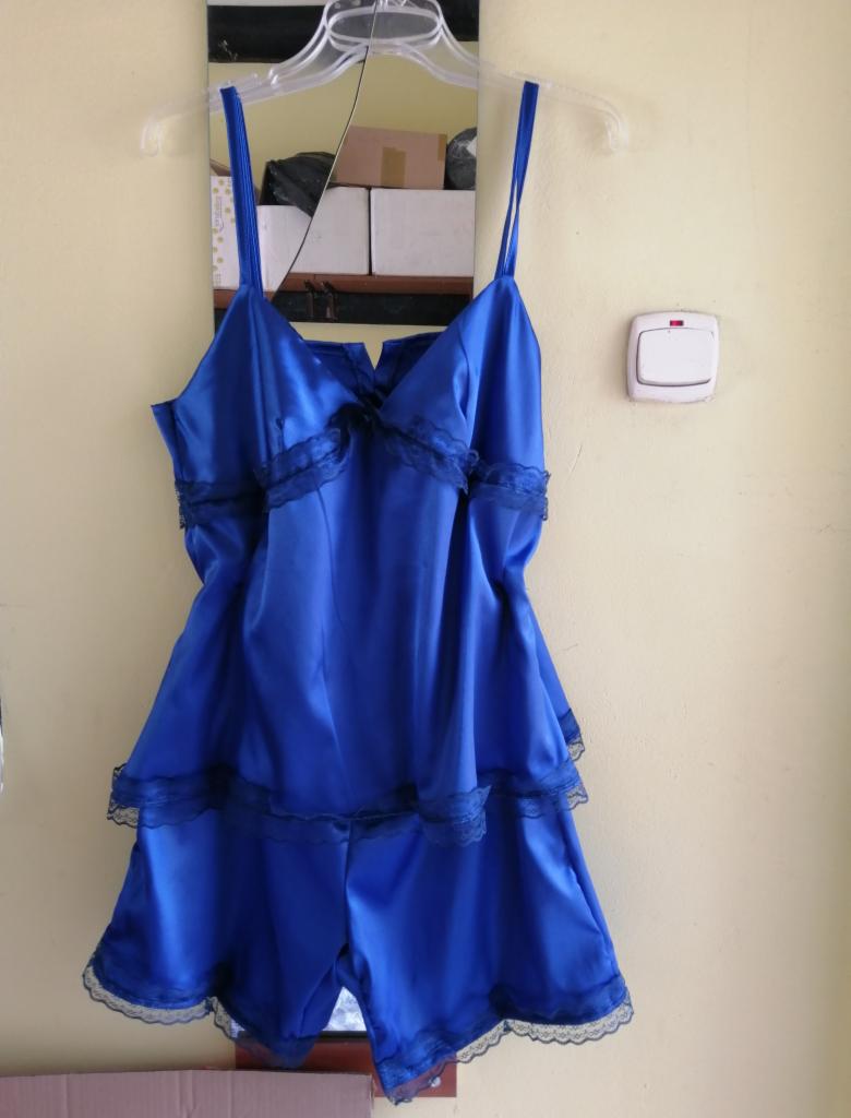 Niebieski satynowy komplet bielizny nocnej z koronkowym wykończeniem, zawieszony na wieszaku przed lustrem i włącznikiem światła na żółtej ścianie.