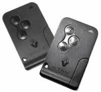 Dwa czarne kluczyki samochodowe Renault Scenic z trzema przyciskami i logo producenta, ułożone obok siebie pod kątem na jasnym tle.