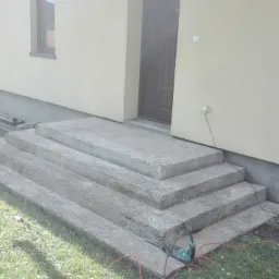 Betonowe schody wejściowe do domu w Rajczy, widoczne narzędzia i przewody elektryczne sugerują trwający proces budowy.