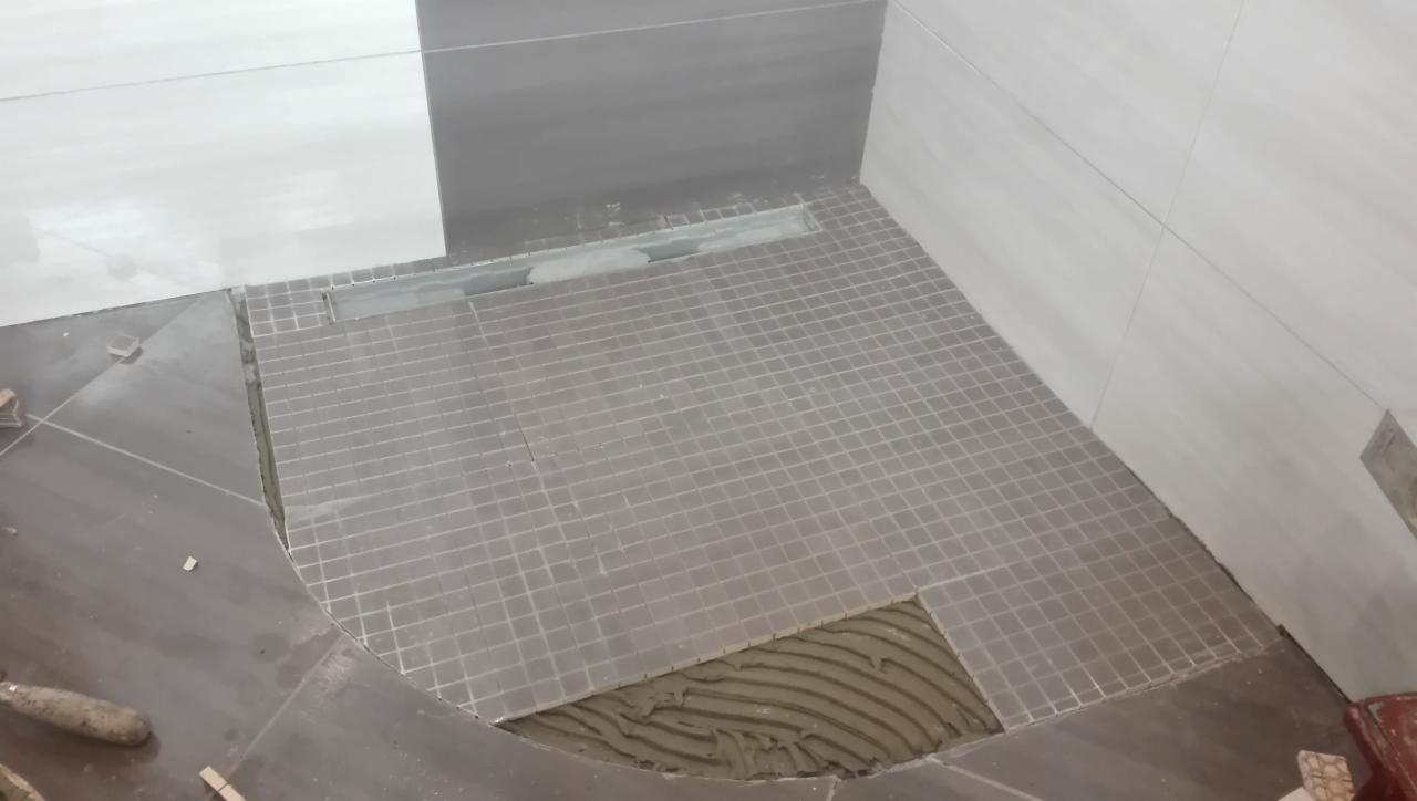 Montaż mozaiki podłogowej w strefie prysznicowej z odpływem liniowym, widoczne niedokończone fragmenty i resztki kleju.