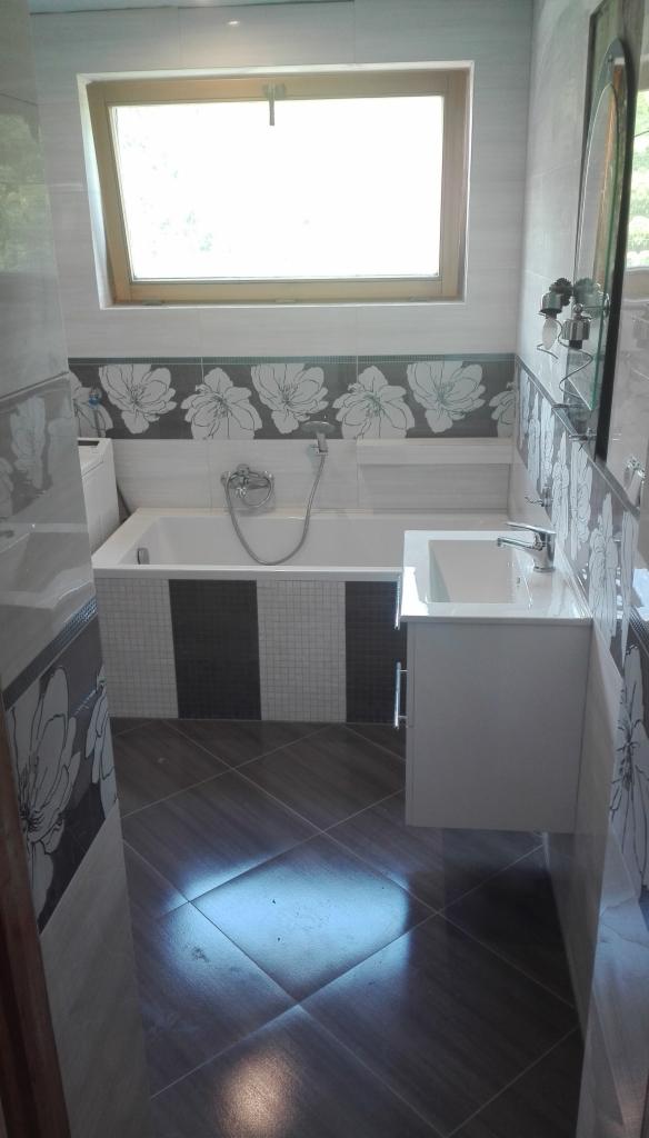 Wykończona łazienka w Rajczy z wanną obudowaną mozaiką, umywalką z szafką i brązowymi płytkami podłogowymi. Na ścianach płytki z motywem kwiatowym.