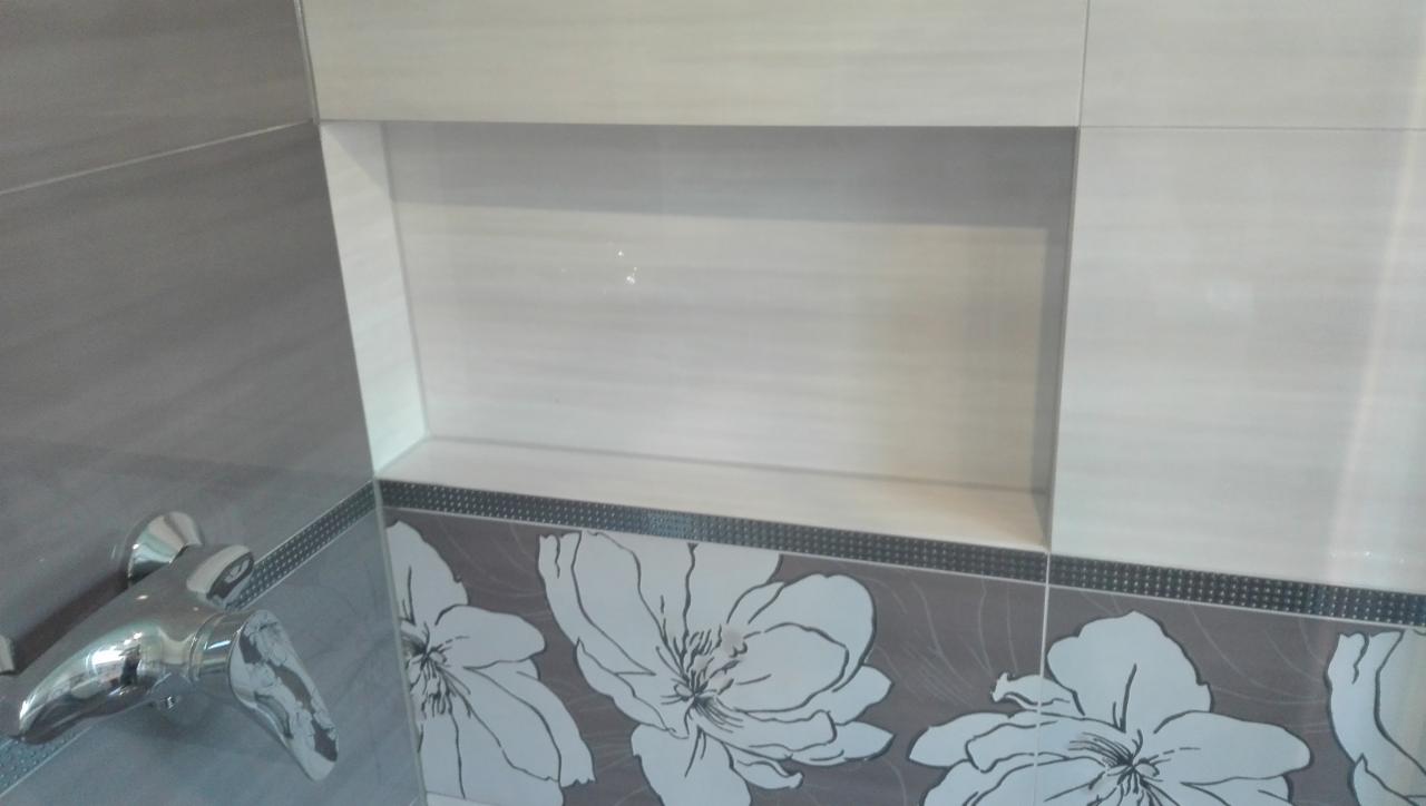 Wykończona łazienka z szarymi i białymi płytkami z motywem kwiatowym i wnęką w ścianie, bateria umywalkowa z kwiatowym wzorem.