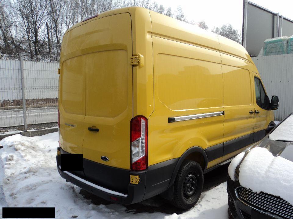 Żółty samochód dostawczy Ford Transit z tyłu, stojący na śniegu, widoczne światła i fragment innego pojazdu.