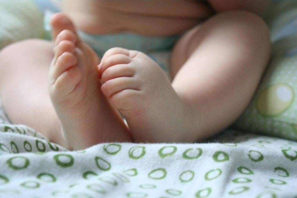 Delikatne stópki niemowlęcia na białej pościeli w zielone wzory, ukazujące wrażliwość i potrzebę opieki, istotne w kontekście szkoleń z pierwszej pomocy.