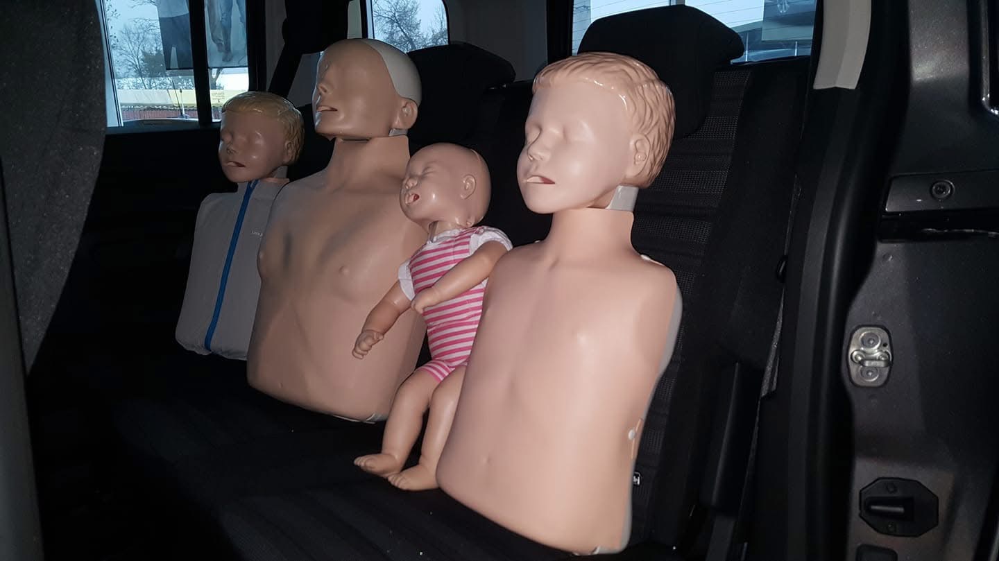 Manekiny do nauki pierwszej pomocy różnych rozmiarów, w tym niemowlę, siedzą na tylnym siedzeniu samochodu. Przygotowanie do szkolenia z zakresu ratownictwa.