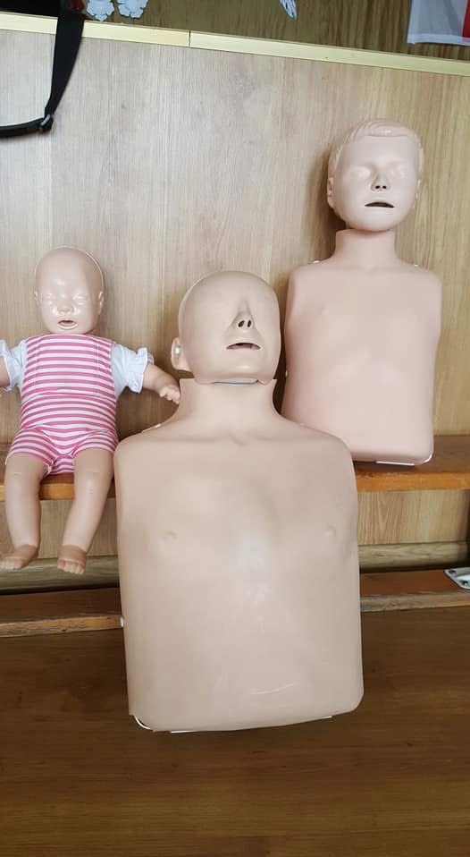Manekiny do nauki pierwszej pomocy: niemowlę w ubranku, tors osoby dorosłej i manekin dziecka na drewnianym tle. Sprzęt do ćwiczeń resuscytacji krążeniowo-oddechowej.