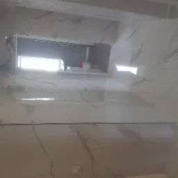 Błyszcząca, marmurkowa okładzina ścian i podłogi w łazience, widok na wnękę z oknem i fragmentem wyposażenia.