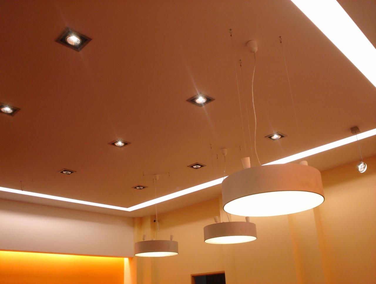 Jasny, beżowy sufit z wpuszczonymi kwadratowymi lampami halogenowymi i liniowym oświetleniem LED oraz dwoma okrągłymi lampami wiszącymi z białymi kloszami.