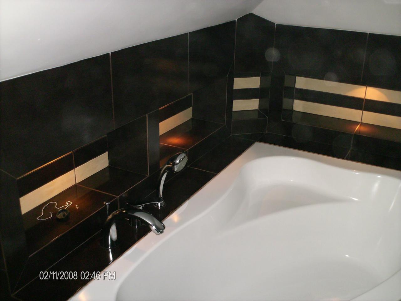 Nowoczesna łazienka z czarnymi płytkami z beżowymi paskami, biała wanna, chromowana bateria i ozdobny łańcuszek na półce.