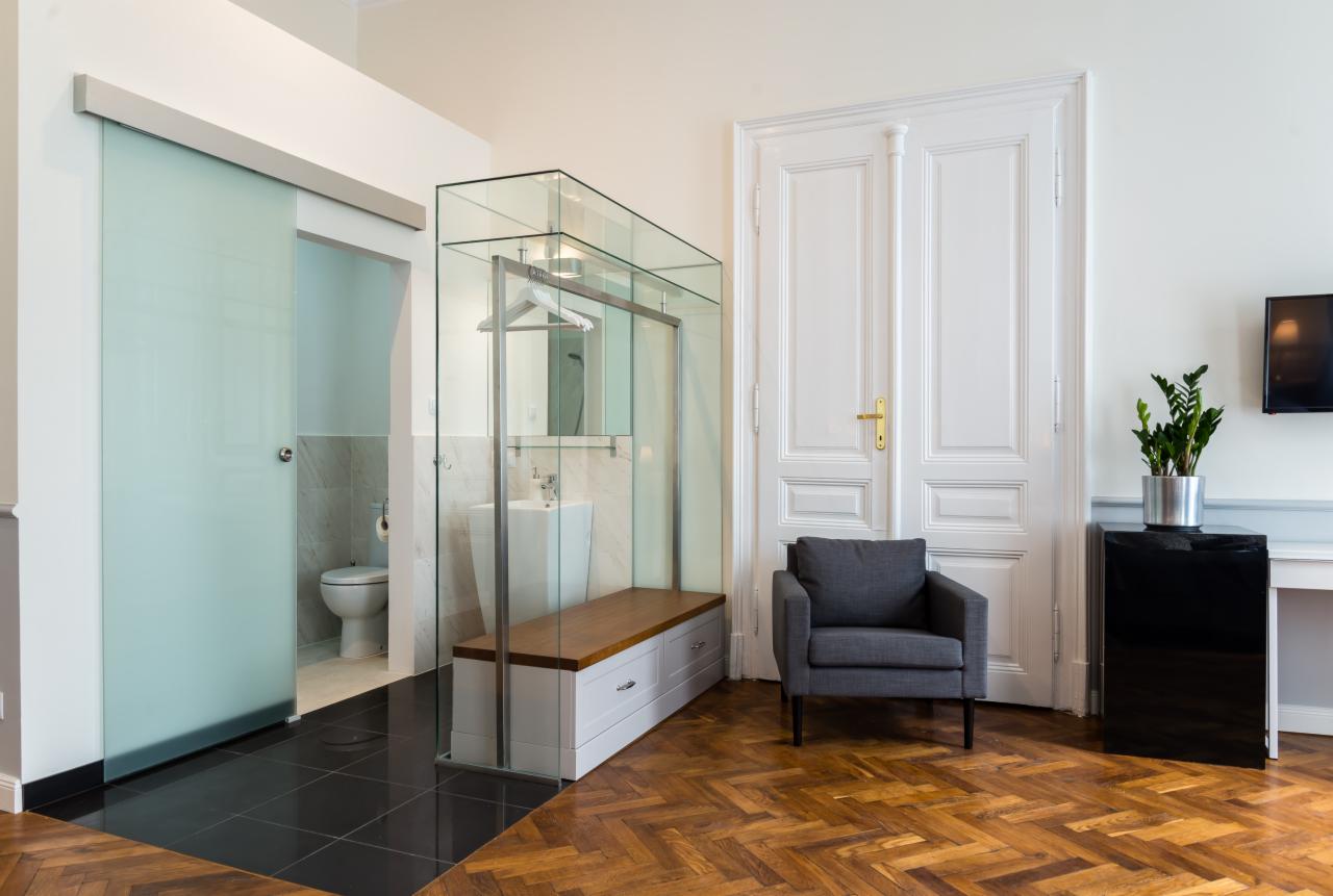 Nowoczesna łazienka z kabiną prysznicową ze szkła i przesuwnymi drzwiami w Krakowie, widoczna umywalka, toaleta i drewniana podłoga w jodełkę.