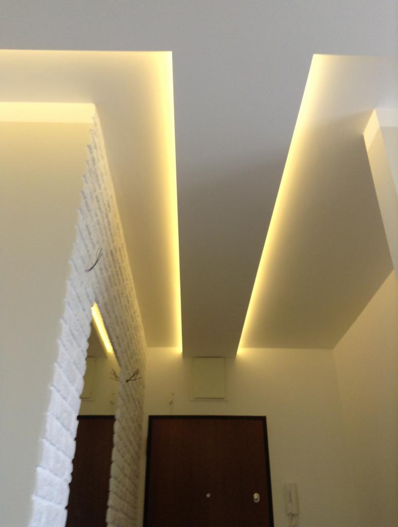 Nowoczesne oświetlenie sufitowe LED w przedpokoju, z dekoracyjną ścianą imitującą białą cegłę i ciemnymi drzwiami.