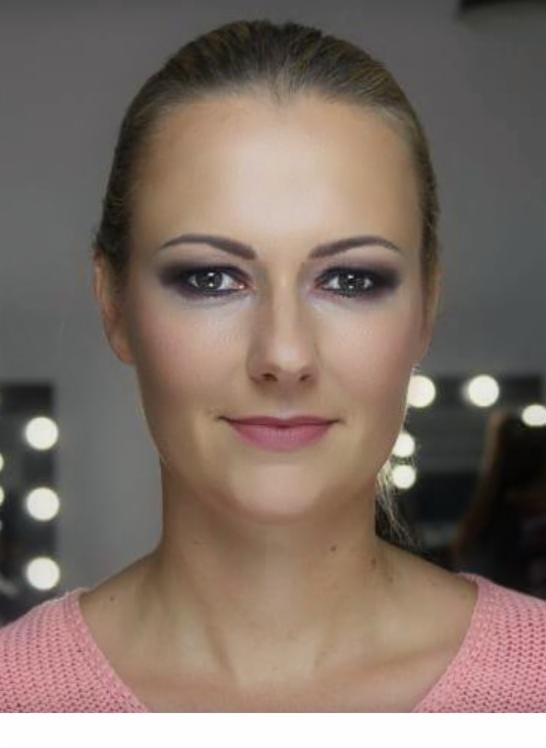Portret kobiety z wieczorowym smoky eye i delikatnym różem na ustach; widoczne oświetlenie lustra do wizażu w tle.