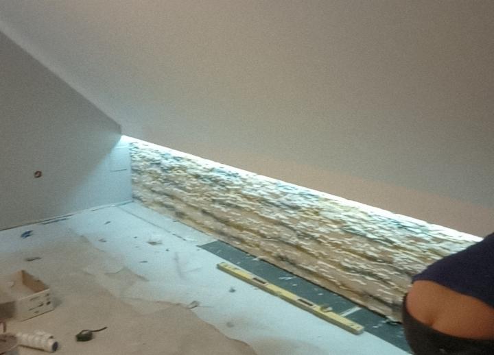 Poddasze w trakcie wygłuszania, widoczna warstwa izolacji na ścianie, poziomica na podłodze, przygotowania do prac wykończeniowych.