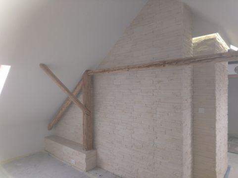Ściana w pokoju na poddaszu wykończona dekoracyjną cegłą w odcieniach bieli, z drewnianymi belkami konstrukcyjnymi w stylu rustykalnym.