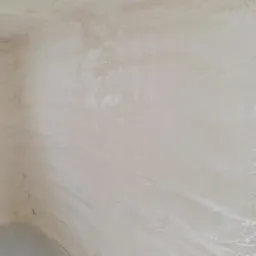 Wnętrze budynku po nałożeniu izolacji natryskowej, widoczne nierówności i struktura piany na ścianach i suficie, szary beton na podłodze w lewym dolnym rogu.