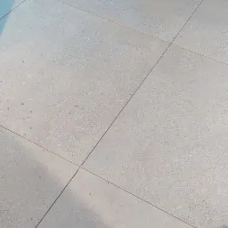 Ułożone, jasnoszare płytki podłogowe z delikatnym wzorem, widoczne fragmenty schodów i kabla w rogu.