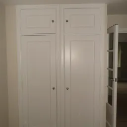 Biała, zabudowana szafa z dwiema parami drzwi, widoczna w mieszkaniu w Piotrkowie Trybunalskim, z otwartymi drzwiami po prawej stronie.