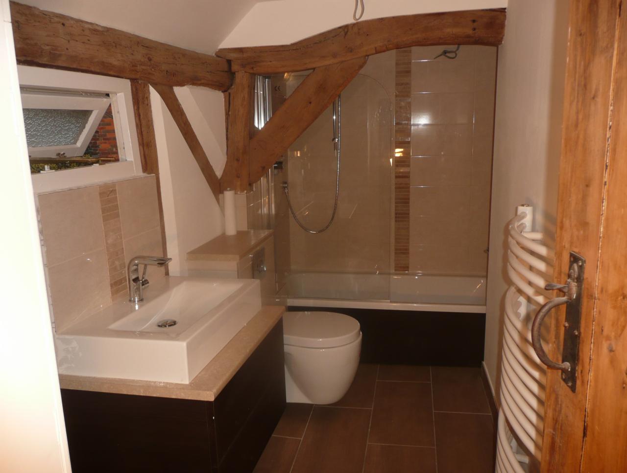 Wykończona łazienka z drewnianymi belkami stropowymi, prostokątną umywalką nablatową, kabiną prysznicową z mozaiką i grzejnikiem drabinkowym obok drewnianych drzwi.