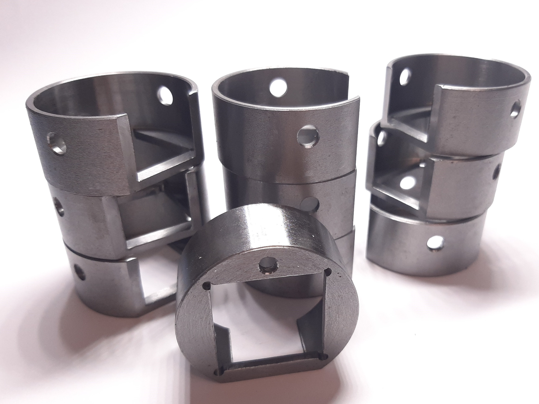 Szczegółowe ujęcie kilku metalowych elementów z otworem i wycięciem, prawdopodobnie tulei lub pierścieni, wykonanych na tokarce, widoczne ślady obróbki.