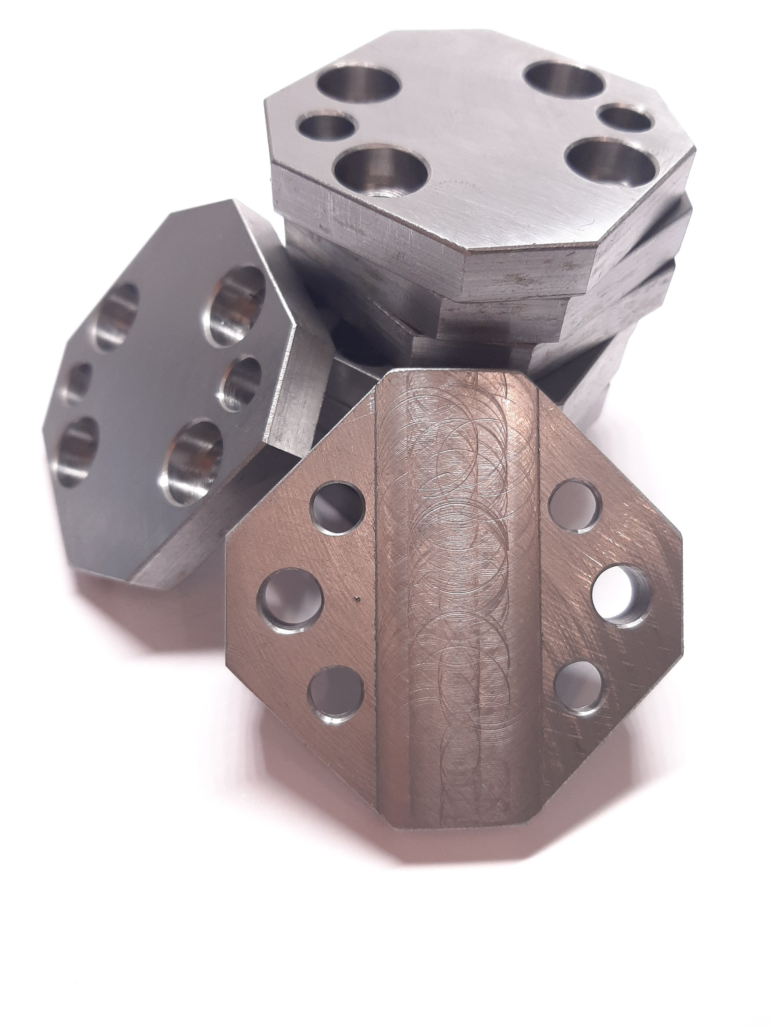 Stos obrobionych, ośmiokątnych, metalowych płyt z otworami, widoczne ślady obróbki skrawaniem na powierzchni jednej z płyt.