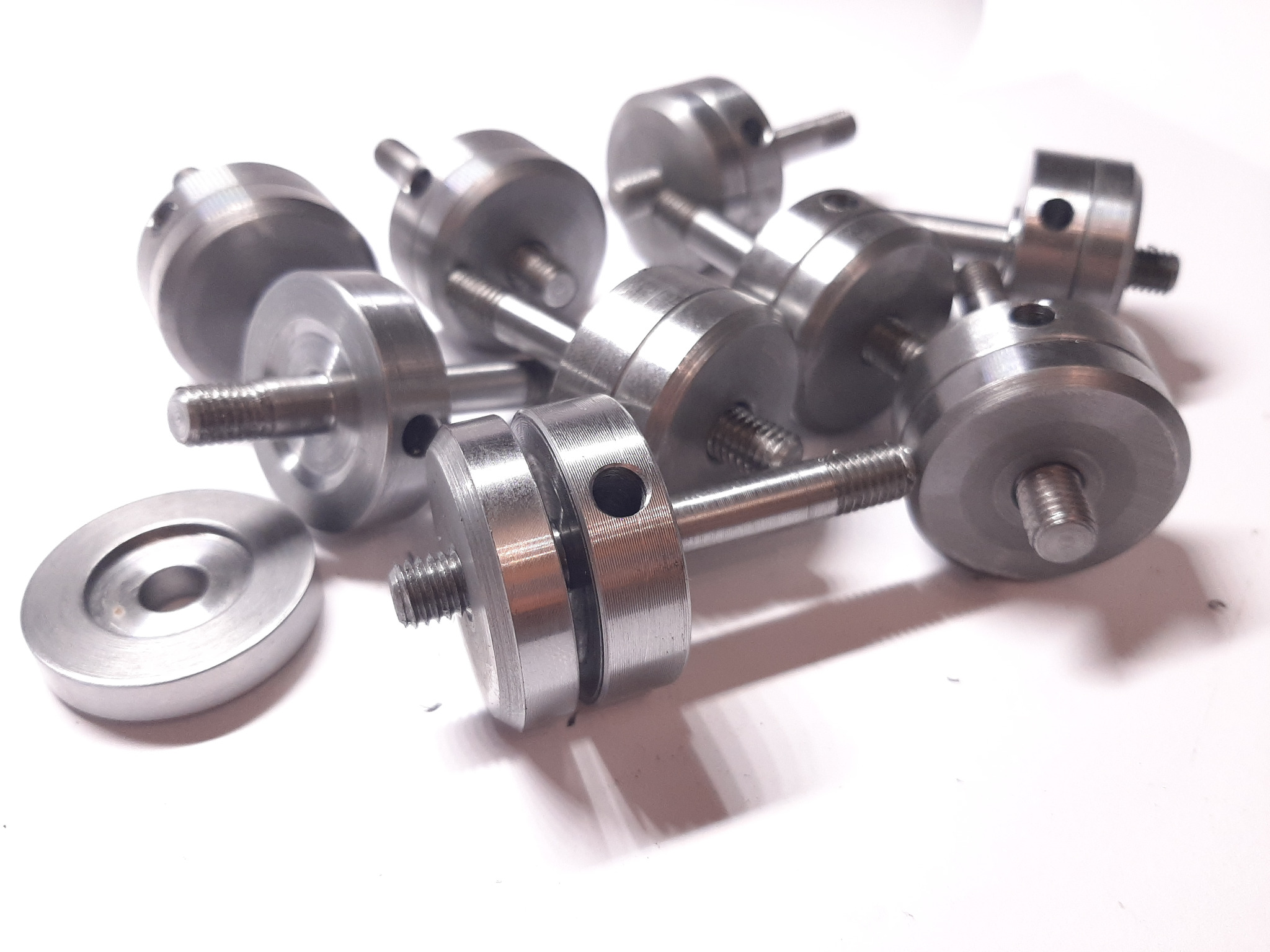 Partie precyzyjnie wykonanych, metalowych elementów z gwintem i otworami, leżących na białym tle, widoczne ślady obróbki.