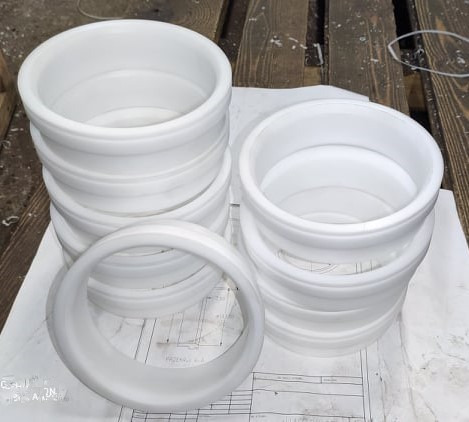 Stos białych, okrągłych elementów z tworzywa sztucznego, ułożonych na stole z widocznymi rysunkami technicznymi. Jeden element leży oddzielnie, eksponując swój okrągły kształt.