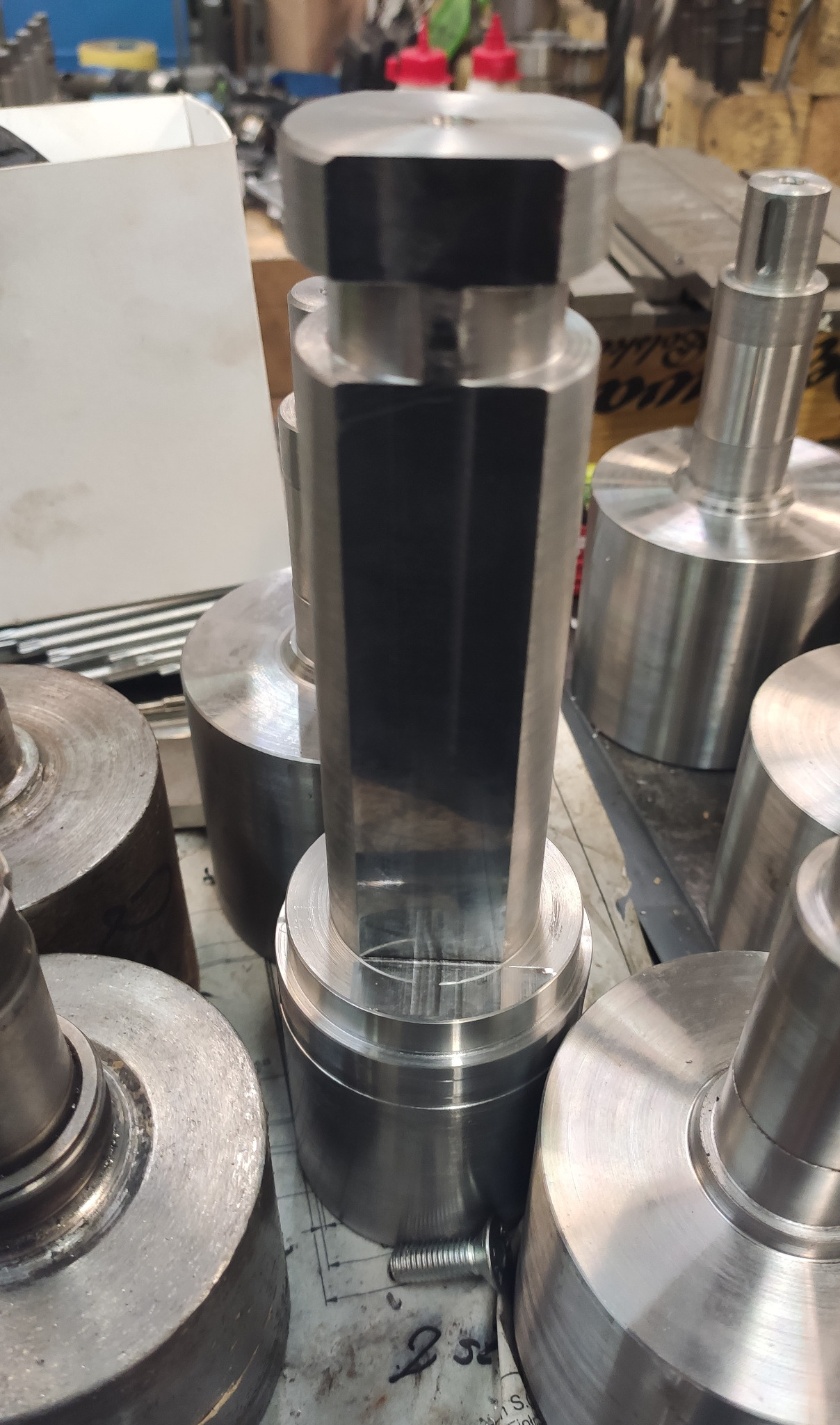 Metalowe elementy po obróbce tokarskiej, widoczne ślady obróbki, zarys techniczny na stole warsztatowym w tle.