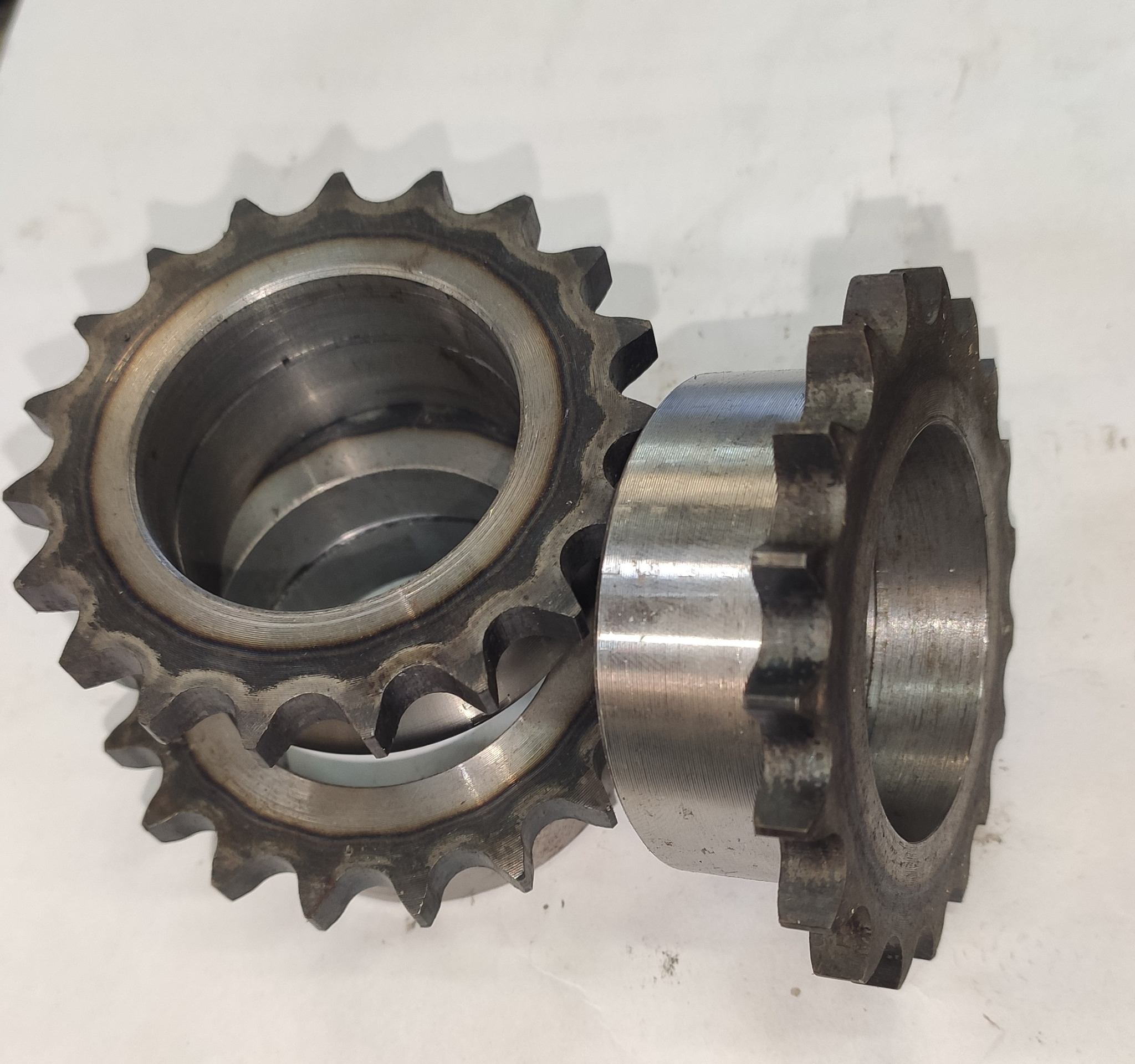 Dwie metalowe zębatki o różnej wielkości, ułożone na białym tle, z widocznymi śladami obróbki i zużycia.