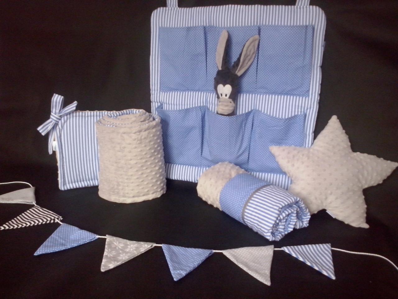 Niebiesko-biały organizer z kieszeniami, pluszowy osiołek, kocyki z fakturą w kropki, poduszka w kształcie gwiazdy i girlanda z trójkątnych proporczyków na czarnym tle.