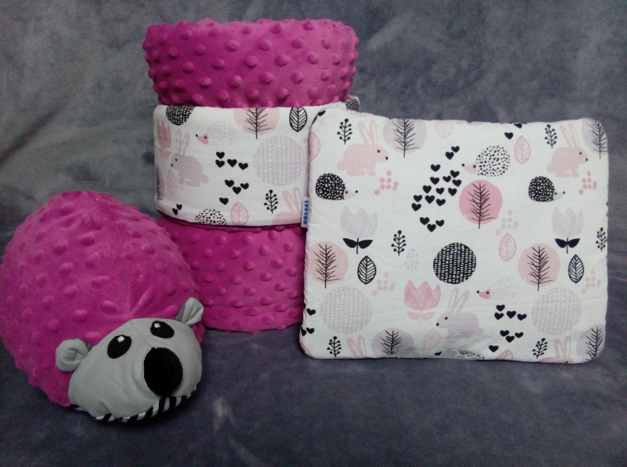 Ręcznie szyte, różowe ochraniacze do łóżeczka dziecięcego z motywem zwierząt i roślin, ułożone na szarym tle.