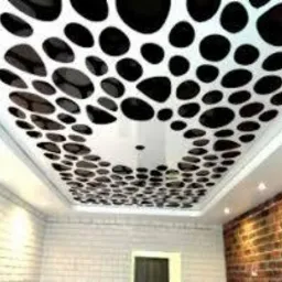 Biały sufit podwieszany z czarnymi, nieregularnymi owalami, częściowo lustrzany, oświetlony punktowymi lampami, ściana z czerwonej cegły w dolnym rogu.