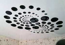Biały sufit z dekoracyjnym wzorem czarnych, okrągłych naklejek ułożonych spiralnie, widoczny fragment tapety w kwiatowy wzór.
