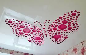 Biały sufit z dekoracyjnym motywem motyla utworzonym z różowych okręgów o różnej wielkości, widoczne fragmenty ściany z tapetą w kwiaty.