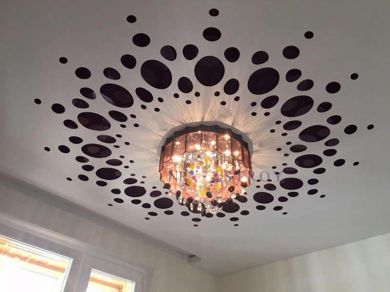 Biały sufit z dekoracyjnymi, ciemnymi okręgami wokół wiszącego, wielobarwnego żyrandola z kryształkami, widok z dołu.