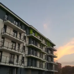 Nowoczesny budynek wielorodzinny w Warszawie z pomalowaną elewacją w odcieniach bieli, szarości i zieleni, widziany pod kątem o zmierzchu.