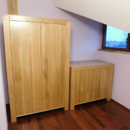 Dębowa szafa dwudrzwiowa i komoda z litego drewna w pokoju na poddaszu z oknem, widoczne usłojenie drewna.