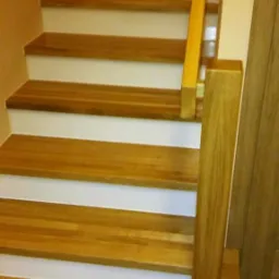 Bieg schodów z drewnianymi stopniami o ciepłym odcieniu, białymi podstopnicami i prostą, jasną balustradą z drewna.