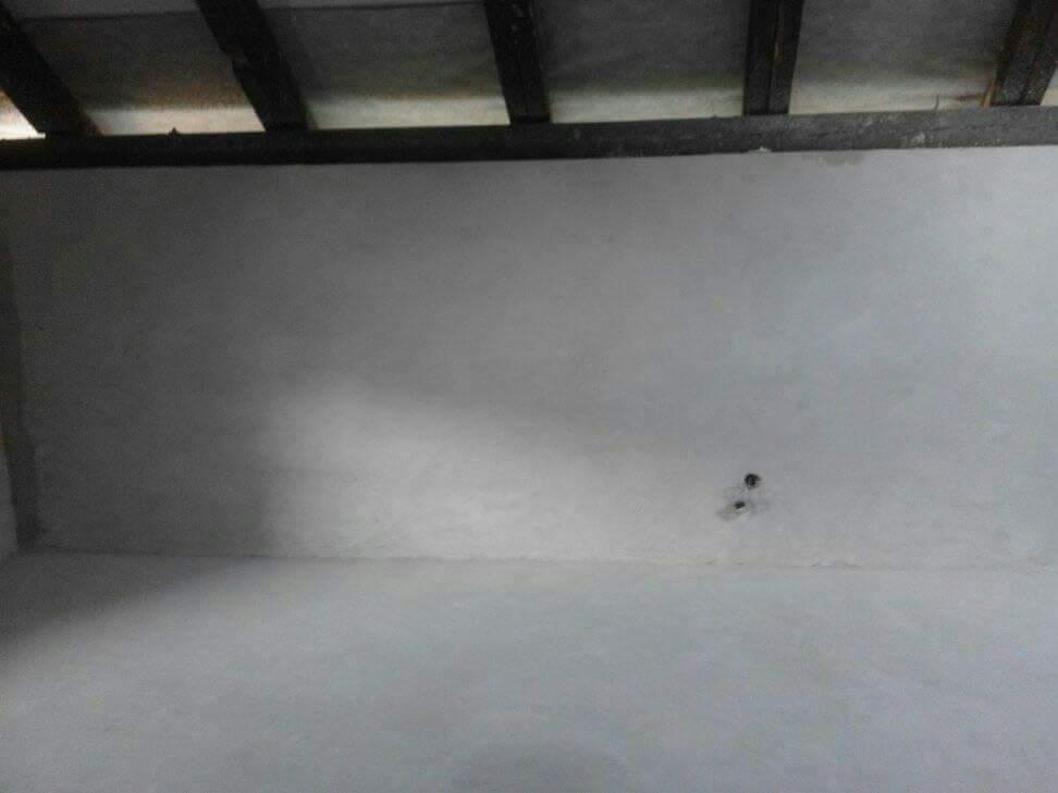 Surowa ściana i sufit po szpachlowaniu w nowym pomieszczeniu z widocznymi drewnianymi belkami stropowymi.